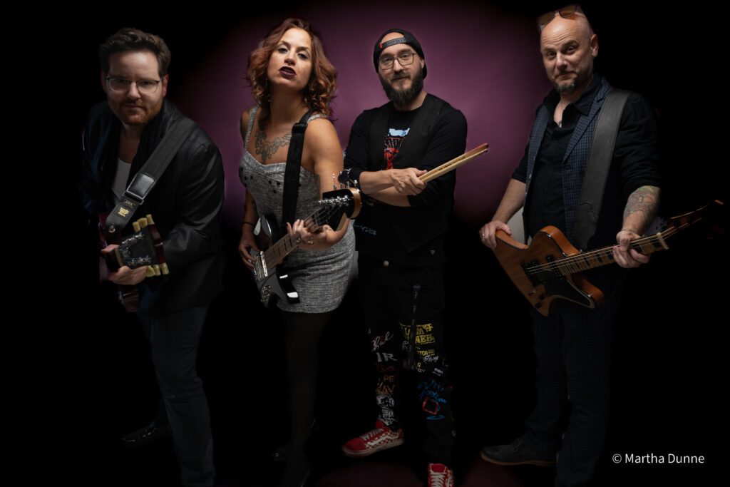 Bellwether Ritual band members posing for a group shot with their guitars in front of a purple wall