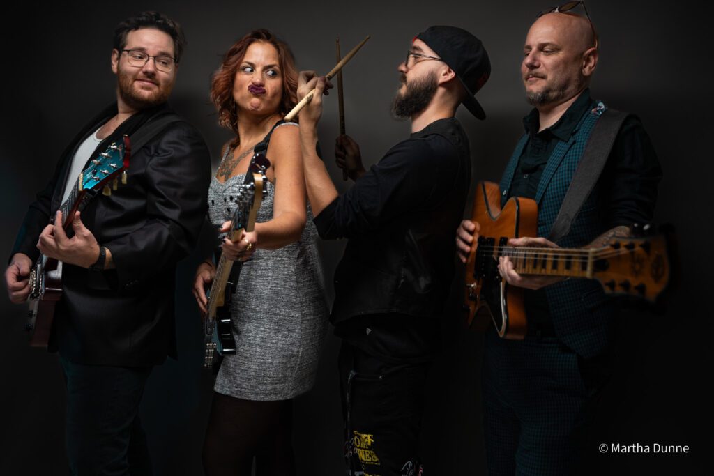 Bellwether Ritual band members posing for a group shot with their guitars in front of a purple wall