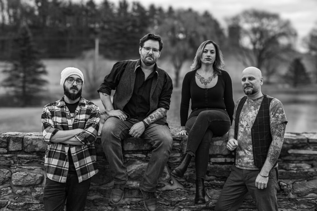 Group shot of the Bellwether Ritual band members sitting on and standing in front of a stone wall at Riverton Recording Studio